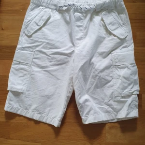 Vita cargo shorts från Polo Ralph Lauren - Snygga vita cargo shorts från Polo Ralph Lauren med elastisk midja. Shortsen har flera praktiska fickor på sidorna och är tillverkade i mjuk bomull, perfekta för varma sommardagar. Klassisk och avslappnad stil med loose fit. Passar till dom som brukar ha medium men även small.