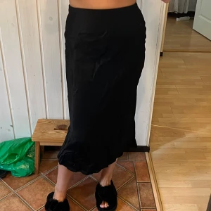 Svart långkjol från H&M i S - Säljer en svart långkjol från H&M i storlek S. Kjolen har en slät, glansig yta och faller snyggt längs kroppen med lätt vågig nederkant. Perfekt för dig som gillar stilrena och enkla plagg med lite extra flow.