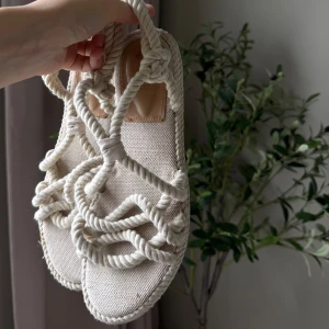 Beiga rep-sandaler från H&M, strl 39 - Unika sandaler från H&M i storlek 39, tillverkade i beige canvas och med grova repdetaljer som ger en cool boho-vibe. Platt sula och öppen tå, perfekta för varma dagar. Snygga att styla med både shorts och klänning.