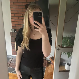 Svart puffärm topp med fyrkantig ringning - Svart topp med trendiga puffärmar och snygg fyrkantig ringning. Modellen är figurnära och har korta ärmar som ger en cool siluett. Perfekt att styla med jeans eller kjol för en stilren look. Från hm. Strl s. Använd 1 gång. Går att pruta 