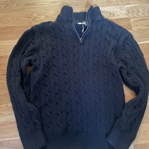 Mörkblå stickad tröja med half zip - Mörkblå kabelstickad tröja från C med hög krage och half zip-dragkedja. Tröjan har långa ärmar och ribbade muddar, perfekt för kyliga dagar. Snygg och klassisk look som funkar till det mesta. Storlek 13-14 158-164 krympt ej 170 