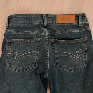 Blå bootcut jeans från Junkyard  - Snygga blå jeans från Junkyard i bootcut-modell med klassisk femficksdesign och coola kontrastsömmar på bakfickorna. Jeansen har en låg midja  och är tillverkade i slitstarkt denimtyg. 