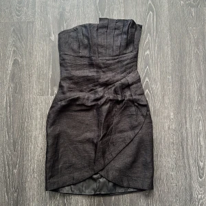 Svart axelbandslös kortklänning från H&M - Snygg svart axelbandslös klänning från H&M med omlott-detalj framtill och veckad överdel. Klänningen är fodrad och har dragkedja baktill för enkel påklädning. Perfekt för dig som gillar stilrena och moderna plagg med en twist. 36 men mer som 34 🌟