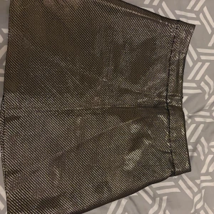 Glittrig kortkjol från H&M i guld - Snygg glittrig kortkjol från H&M i guld med diskret randigt mönster. Kjolen har en rak passform och dragkedja i sidan. Perfekt för dig som vill sticka ut med metallic vibes och cool stil.