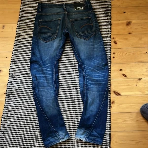 Blå faded jeans från G-Star RAW - Säljer ett par snygga blå jeans från G-Star RAW med coola detaljer på bakfickorna och galna fades. Jeansen har normal passform och är tillverkade i klassisk denim. Storlek 30/32 och passar straight. Sjuka fades!