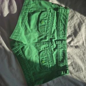 Gröna shorts med fickdetaljer - Snygga gröna shorts i bomull med coola fickor framtill och matchande gröna knappar. Modellen är kort och har bälteshällor, perfekt för dig som gillar färg och vill sticka ut. Knappt använda, säljer dem för att det för för små.