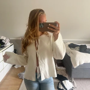 Vit kofta med knyt framtill - Säljer en vit blus med långa ärmar och tre knyt framtill från Gina, den har en liten tråd som synd där fram men inget man tänker på, va så när jag köpte den, typ oanvänd