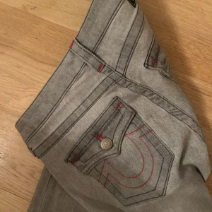 True Religion Joey grå flare jeans - Grå jeans från True Religion, modell Joey Low Rise Flare. Snygga röda sömmar och klassiska bakfickor med lock och knapp. Låg midja och utsvängda ben, Perfekta för dig som gillar statement-jeans ❤️