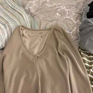 Beige ribbad kofta från 157 - Säljer en beige kofta från 157 med ribbad struktur och v-ringad hals. Koftan har en knapp framtill och långa ärmar. Perfekt att slänga på sig när det är lite kyligt ute. Enkel och stilren design som funkar till många outfits.