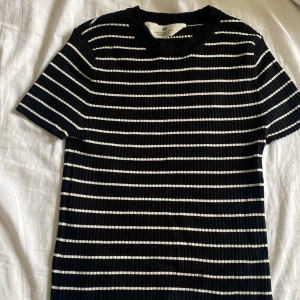 Randig ribbad topp från H&M - Svart och vit ribbad topp från H&M med horisontella ränder. T-shirttyp med rund hals och korta ärmar. Mjuk och stretchig känsla, perfekt till jeans eller kjol. Enkel men snygg design som funkar året runt.