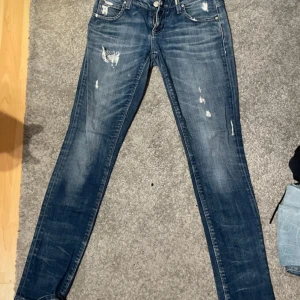 Blå skinny jeans från ONLY - Mörkblå skinny jeans från ONLY med slitna detaljer och snygga slitningar framtill. Klassisk femficksmodell med dragkedja och knapp. Jeansen har låg midja och är tillverkade i stretchigt denim för en tight passform.
