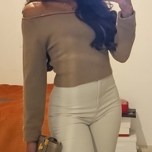 Beige offshoulder stickad tröja - Snygg beige stickad tröja med offshoulder-design och långärmade ärmar. Tröjan har en ribbad struktur och sitter tajt över axlarna för en trendig look. Perfekt att matcha med höga byxor eller kjol för en stilren outfit.