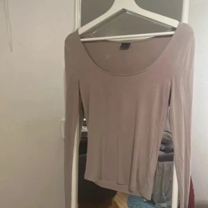 Beige långärmad topp med rund hals - En enkel och stilren beige långärmad topp med rundad, djup urringning. Tunn och mjuk i materialet, perfekt att styla med jeans eller kjol. Snygg baströja som funkar året runt och är lätt att matcha med andra plagg.