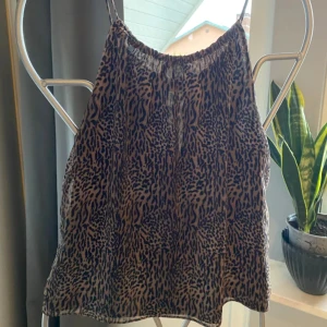Leopardmönstrad topp från Mango!    - Säljer en snygg  frånMango  med leopardmönster i beige och svart. Toppen har tunna axelband, lös passform och en liten knytning framtill vid halsen. Perfekt för dig som vill sticka ut med ett djurmönstrat plagg! Den är fodrad! Är i nyskick! 