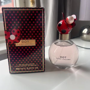 Dot parfym från Marc Jacobs 100ml - Dot från Marc Jacobs är en söt parfym i en rund glasflaska med ljusrosa vätska. Locket är rött med svarta prickar och dekorerat med pärlliknande detaljer, inspirerat av en nyckelpiga. Kommer med en svart och rödprickig kartong. 100 ml Eau de Parfum.