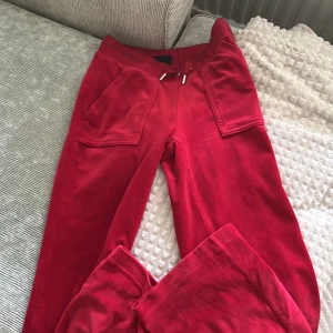 Röda mjukisbyxor Juicy Couture XS - Riktigt snygga röda mjukisbyxor från Juicy Couture i storlek XS. Byxorna har breda ben, stora fickor framtill, snörning i midjan och broderad JC-logga på ena fickan. Mjukt och skönt material som ger en lyxig känsla.