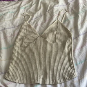 Beige ribbad linnetopp från Zara - Säljer en beige ribbad linnetopp från Zara med smala axelband och v-ringad skärning. Toppen har en figurnära passform och är tillverkad i ett mjukt, stretchigt material som känns skönt mot huden. Perfekt att styla med jeans eller kjol för en enkel och snygg look. Storlek M/L tycker jag.