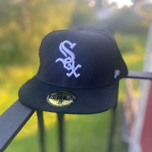 Svart New Era White Sox 59FIFTY keps - Snygg svart 59FIFTY keps från New Era med White Sox-logga broderad i vitt framtill. Klassisk basebollmodell med rak skärm och MLB-logga baktill. Tillverkad i tålig polyester, perfekt för dig som gillar sportig streetstyle.