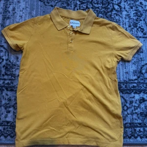 Gul pikétröja från D.M.D by denim day - Snygg gul pikétröja från D.M.D by denim day i klassisk modell med krage och tre knappar framtill. Det finns några väldigt små fläckar som knappt syns, ni kan kolla på fjärde bilden.