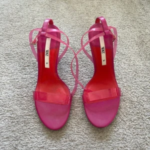 Rosa klackade sandaler från Zara - Snygga rosa sandaler från Zara med transparenta remmar och höga klackar. Skorna har smal rem över tårna och tunna remmar som knyts runt vristen. Perfekta för dig som vill sticka ut med färg och stil. 