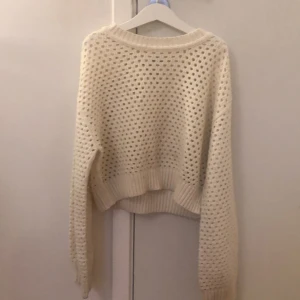 Vit stickad tröja från H&M - Säljer en vit  stickad tröja från H&M med hålmönster och ribbade muddar. Tröjan har en avslappnad passform och långa ärmar, perfekt för lager-på-lager. Enkel att styla med både jeans och kjol.