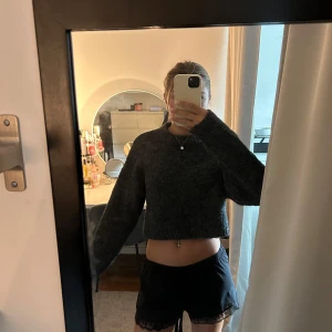 Mörkgrå croppad stickad tröja - Mysig mörkgrå croppad stickad tröja med lång ärm och rund halsringning. Perfekt för lager-på-lager och passar till både jeans och kjol. Enkel och stilren design som är lätt att matcha.