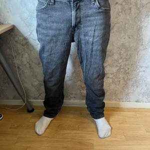 Grå Lee jeans med rak passform - Säljer ett par grå jeans från Lee med klassisk femficksdesign och raka ben. Jeansen har tydliga Lee-detaljer på knapp och bakficka, samt en snygg tvättad finish. Materialet är robust denim som ger en cool vintagekänsla. Hör av dig vid minsta fundering pris ej hugget i sten! W32 L30