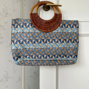 Mönstrad shoppingväska med trähandtag - Säljer en unik shoppingväska med geometriskt mönster i blått, beige och brunt. Väskan har stora runda handtag i trä och insida med fickor och dragkedja. Perfekt för dig som vill sticka ut med en färgglad och bohemisk accessoar.