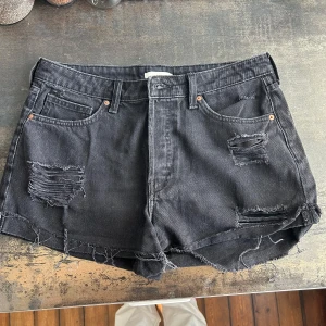 Svarta jeansshorts med slitningar H&M - Svarta jeansshorts från H&M i storlek 42. Modellen har fransiga kanter och flera slitna detaljer framtill!
