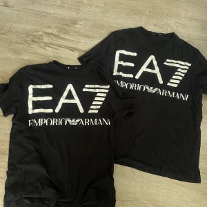 2 Svarta EA7 Emporio Armani t-shirt - Svart t-shirt från EA7 Emporio Armani med stor vit logga och tryck framtill. Klassisk rund hals och korta ärmar. Tillverkad i mjuk bomull som känns skön mot huden. Perfekt för dig som gillar streetwear och vill sticka ut med en ikonisk logga. Säljs 2 pack