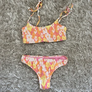 Blommig bikini i rosa och gul - Superfin bikini med smockat tyg och blommigt mönster i rosa, gul, orange och vitt. Justerbara axelband. Från HM