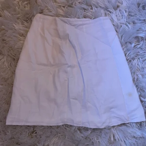 Vit kortkjol från BikBok XS - Vit kortkjol från BikBok i storlek XS. Kjolen har en enkel och stilren design med en liten slits framtill som ger en snygg detalj, det är linne tyg , det finns dock en liten defekt högst upp på slitsen men de är inget stort eller något som man tänker på och går säkert att fixa !! 💕💕