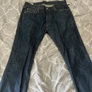 Levi's 501 mörkblå jeans - Klassiska Levi's 501 jeans i mörkblå denim med raka ben och femficksmodell. Byxorna har den ikoniska röda Levi's-taggen på bakfickan och läderpatch i midjan. Snygga kontrastsömmar och tidlös passform som funkar till allt. Storlek 33w -32h