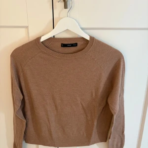 Beige stickad tröja från mango - En stilren beige stickad tröja från mango i storlek XS. Tröjan har rund halsringning, långa ärmar och en klassisk passform. Perfekt för lager-på-lager och enkel att matcha med jeans eller kjol.
