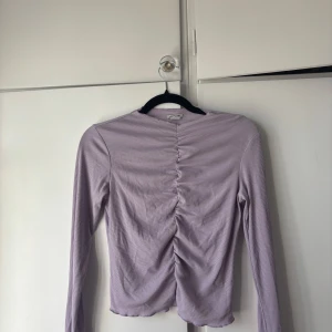 Ljuslila ribbad topp med rynk - Supersöt ljuslila långärmad topp från Monki med ribbad struktur och snygg rynkdetalj framtill. Perfekt att styla med jeans eller kjol för en trendig look. Mjuk och stretchig i materialet för extra komfort. Hör av dig om du vill ha fler bilder eller ha frågor!