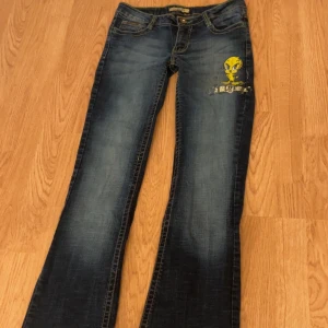 LOT29 jeans med Tweety-tryck - Mörkblå flare jeans från LOT29 med coolt gult Tweety-tryck på ena benet. Klassisk femficksmodell med kontrastsömmar och låg midja💛Midjemått: 37 cm, Innerbenslängd: 76 cm