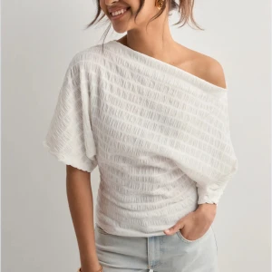 Vit offshoulder topp med struktur - Säljer en vit topp med snyggt strukturerat tyg och offshoulder-design. Toppen har korta, vida ärmar och en avslappnad passform som ger en cool och trendig look. Perfekt att matcha med jeans för en stilren outfit. Ny utan prislapp🩶