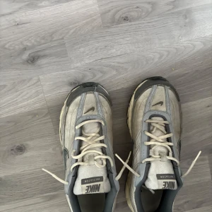 Nike Initiator sneakers i grått och vitt - Nike Initiator sneakers i grått och vitt med klassisk swoosh på sidan. Skorna har mesh- och syntetpaneler, snörning och en chunky sula. Perfekta för dig som gillar retrovibbar och sportig stil.