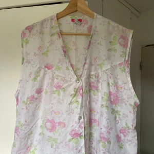 Blommig ärmlös långklänning - Söt långklänning med blommigt mönster i rosa och grönt på vit botten. Klänningen är ärmlös, har v-ringning och knäpps framtill med knappar. Två stora fickor framtill och en avslappnad passform gör den både chill och romantisk.