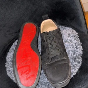 Svarta sneakers från Christian Louboutin - Snygga svarta sneakers i mocka från Christian Louboutin med den ikoniska röda sulan. Skorna har rund tå, svarta snören och diskreta detaljer. Perfekta för dig som vill ha en stilren men ändå lyxig look.