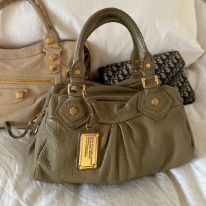 Snygg khaki Q Classic Baby Groove väska! - Köp helst via min vinted, billigare pris pga lägre avgifter @juliavallberg 🤍  Snyggaste khaki färgade handväskan i äkta läder från Marc by Marc Jacobs. Den ikoniska modellen Q Classic Baby Groove! En populär och eftertraktad vintagemodell med gulddetaljer och dubbla handtag. Väskan är i fint skick och är mycket välbevarad, en fläck vid dragkedjan som syns på bilden🤍  Mått: 34x18x12 cm (undersida) Kan hämtas hemma hos mig i Nacka eller skickas 🤍