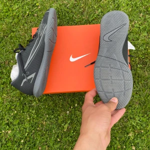 Nike Mercurial  - Snygga Nike Mercurial fotbollsskor i svart och grått med coola grafiska detaljer på sidan. Skorna har snörning och en slitstark syntetisk ovandel samt mönstrad sula för bra grepp. Perfekta för dig som vill sticka ut på planen.