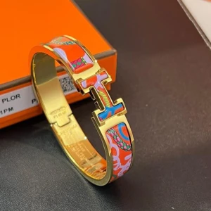 Färgglatt H-armband från Herms - Snyggt armband i guldton från Herms med ikoniskt H-spänne. Armbandet har färgglada detaljer i rött, blått, rosa och orange med mönstrade inslag. Perfekt statement piece för att lyfta din outfit.