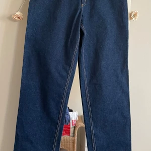 Mörkblå jeansbyxor från Oggi - Snygga mörkblå jeansbyxor från Oggi med klassisk femficksdesign. Byxorna har en rak passform och är tillverkade i slitstarkt denim. Byxor är hög midja,storlek på midjan är ca 37cm . Längd från insidan av byxan är 87cm . Sidor av benen är 114cm .köpt år 2003 helt oanvänd.nypris 1600 kr . Jag vill ha 550kr.kan möta er i Stockholm utanför Åhléns i T-Central 
