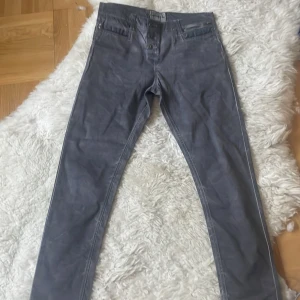 Grå byxor från Copenhagen Luxe - Snygga grå byxor från Copenhagen Luxe med dragkedjedetalj vid fickan och knappar framtill. Byxorna har en modern stil och passar perfekt för en stilren look. Midjemått 85 cm, Innebensmått 73 cm.