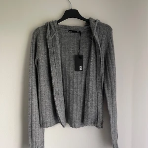 Grå ribbad hoodie från 157 - Säljer en stilren grå ribbad hoodie från 157. Tröjan har dragkedja och en mysig huva, perfekt för kyliga dagar. Den är långärmad och har en normal passform. Oanvänd