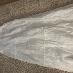 Vit långkjol från Gina  - Säljer en elegant vit långkjol från Gina. Kjolen har en luftig och bekväm passform, perfekt för varma dagar. Den är tillverkad i ett lätt material som ger en fin rörelse. Perfekt för en stilren look! Lappen är kvar, aldrig använt 