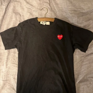 Svart t-shirt från Comme des Garçons (S) - Säljer en svart t-shirt från Comme des Garçons med det ikoniska röda hjärtat på bröstet. Den är i storlek S men sitter som XS. Köpt på paul and friends i stockholm.