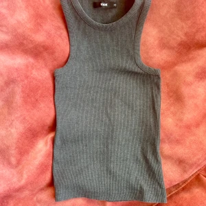 Grå ribbad linnetopp från Bikbok - Säljer en stilren grå ribbad linnetopp från Bikbok. Perfekt för lager-på-lager eller att bära som den är. Toppen har en klassisk rund halsringning och ärmlös design.