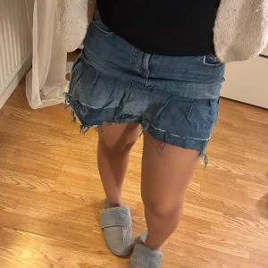 Blå jeanskjol med volang - Säljer en cool blå jeanskjol med volangdetaljer och råa kanter. Kjolen har en kort längd och klassisk jeansdesign med fickor och bälteshällor. Perfekt för en avslappnad stil.